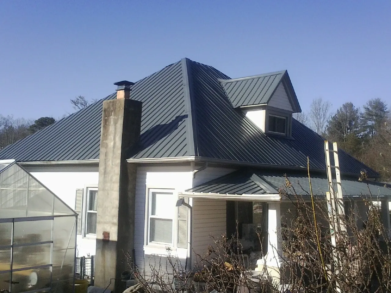 Dark blue standing seam metal roof on a white farmhouse with dormer — Slate & Tile Roof Repair by Roofing Brothers in Brunson