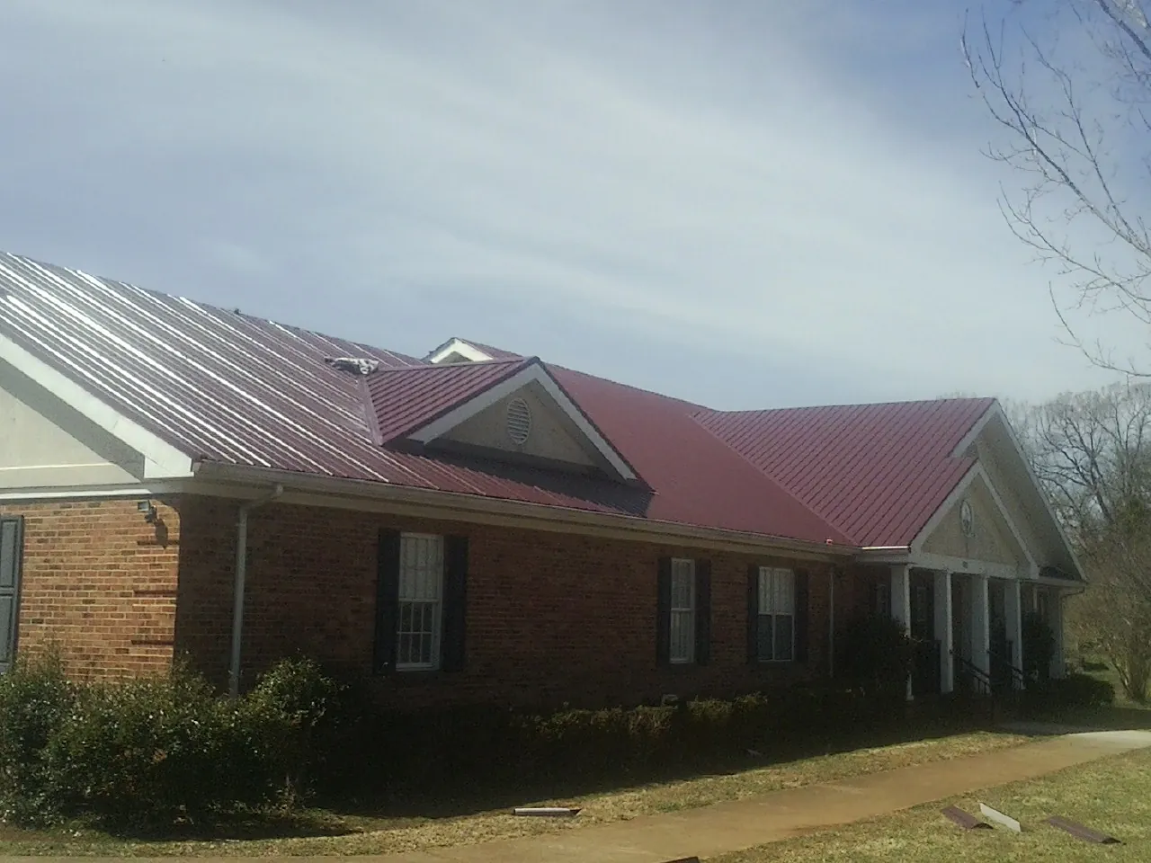 Red metal roof with gabled entries on a long brick building, from a Hail Damage Roof Repair job in Brunson