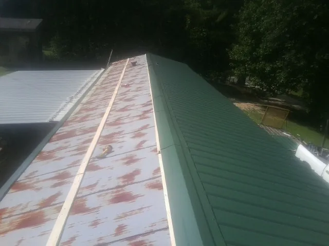 Old rusted panels beside newly installed green metal roofing — Wind Damage Roof Repair by Roofing Brothers in Brunson