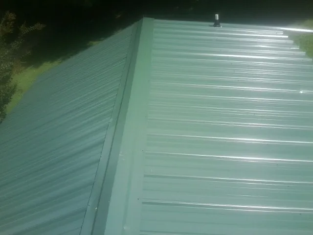 New green metal panels meeting at the ridge of a roof — Flat Roof Repair work by our crew in Brunson