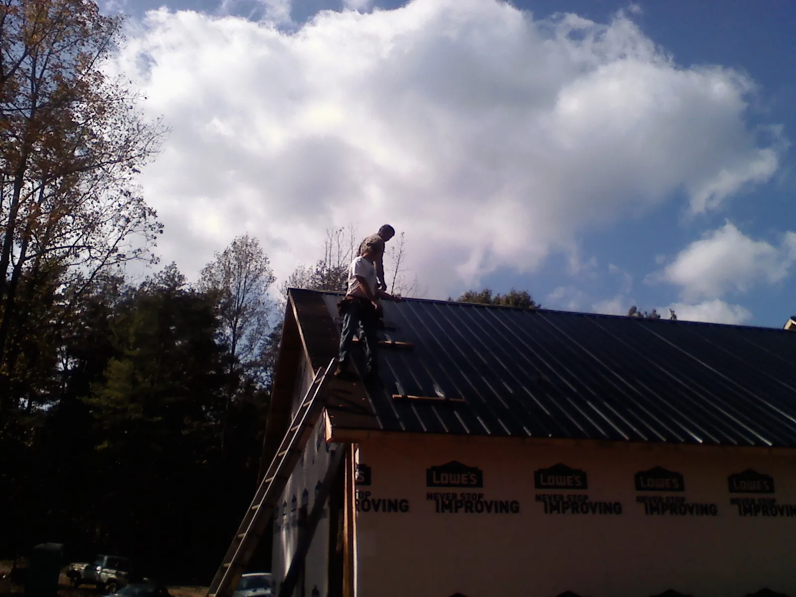 Roofer fastening dark metal panels high against a cloudy sky, from a Roof Inspection job in Brunson