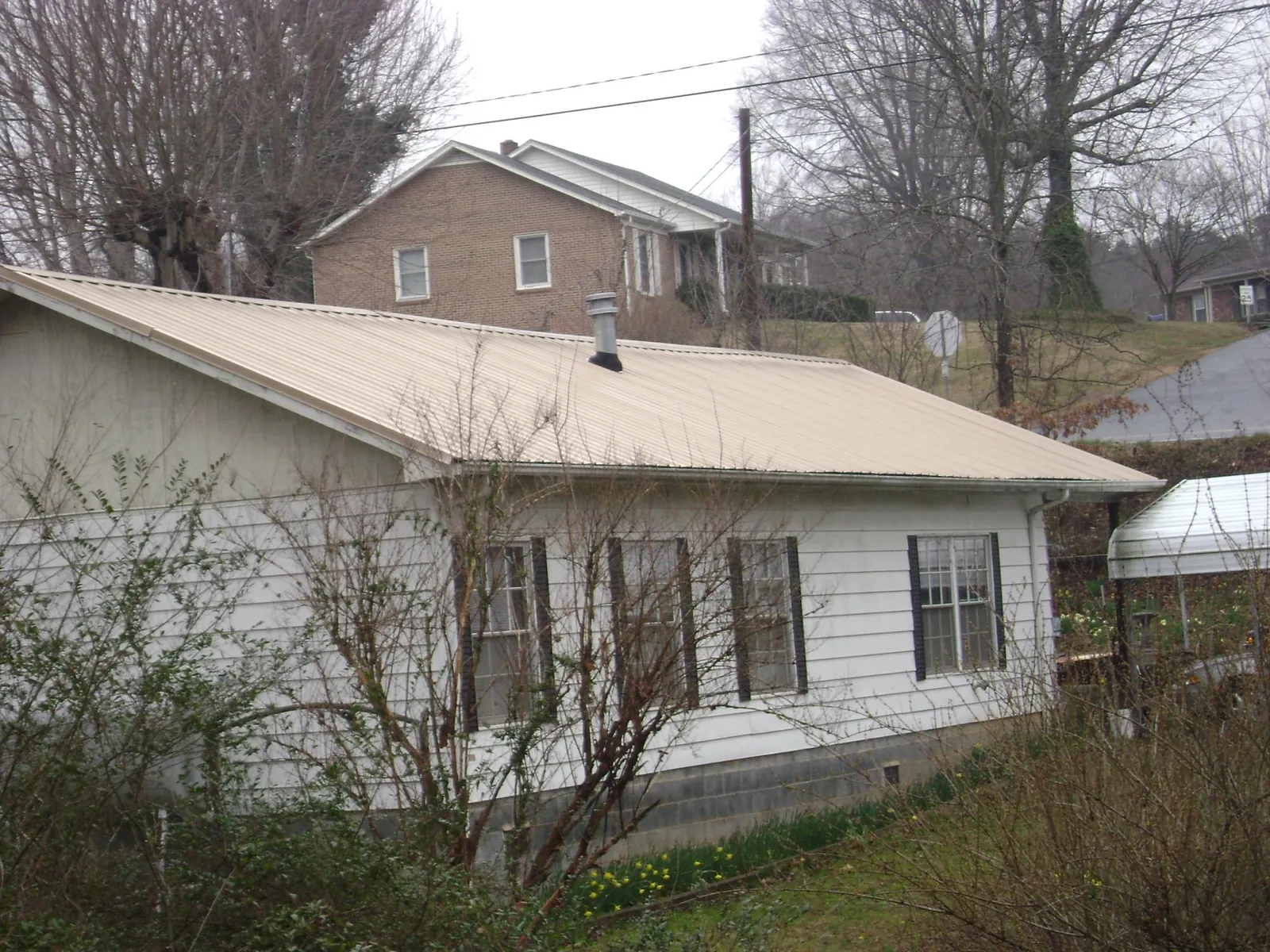 Tan metal roof on a white sided house set into a hillside — Commercial Roofing by Roofing Brothers in Brunson
