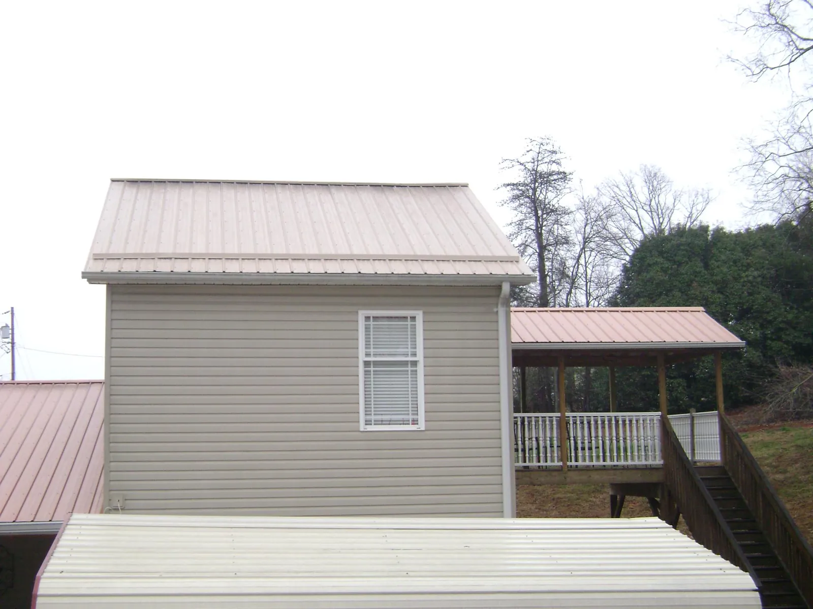 Tan metal roofs on a two story addition and attached porch, from a Roof Replacement job in Brunson
